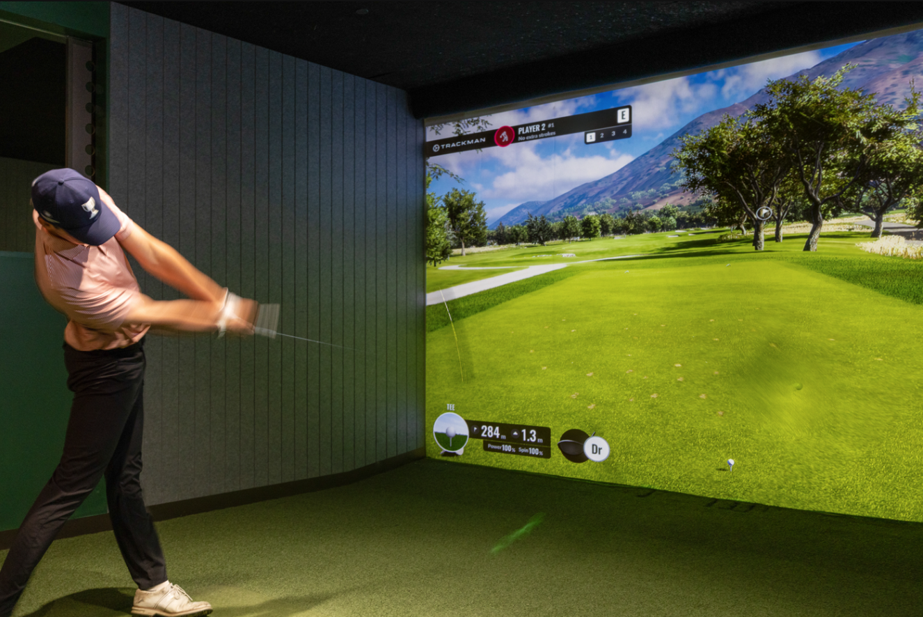 Golfer driving with a full course view on the GolfSpace simulator screen.