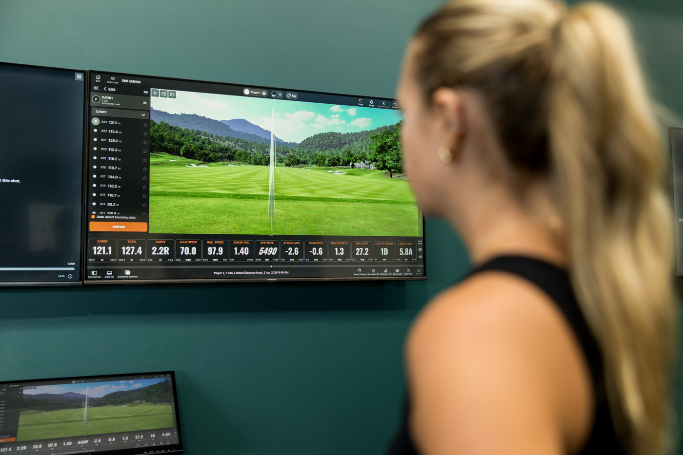 Golfer reviewing a full TrackMan shot-analysis dashboard: club speed, ball speed, smash factor, spin and attack angle.
